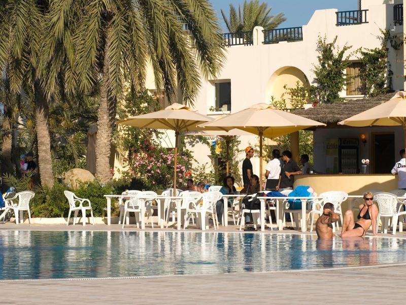 Hotelpool mit Palmen, weißen Stühlen und Sonnenschirmen, Gäste entspannen am Wasser.