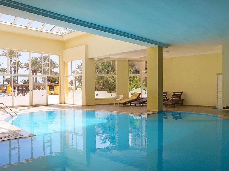 Ein überdachter Innenpool mit großen Fenstern und mehreren Liegestühlen.