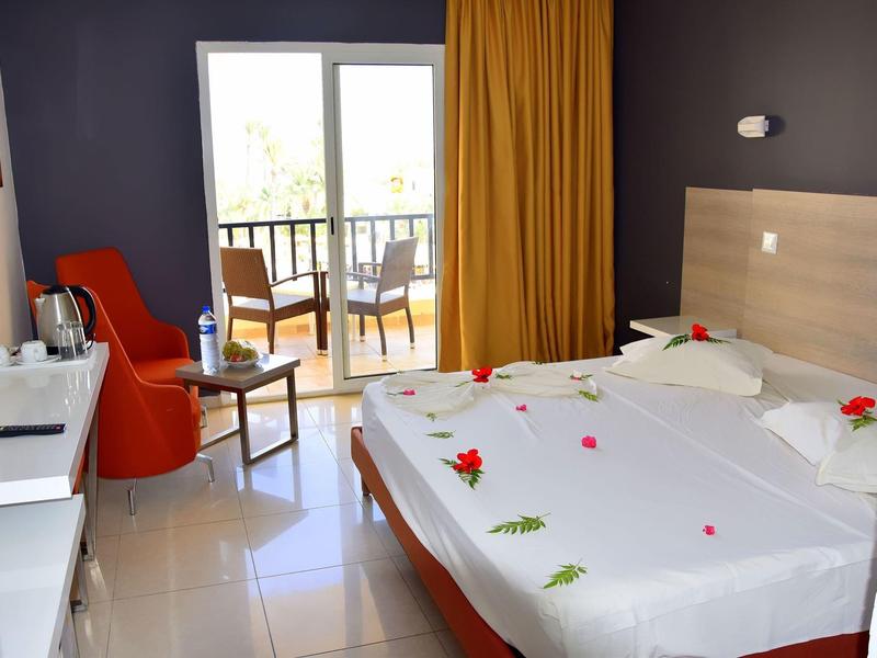 Modernes Hotelzimmer mit Doppelbett, orange Stuhl, Balkon und gelben Vorhängen.