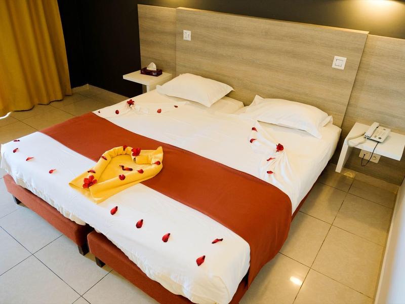 Doppelbett mit weißer Bettwäsche, roten Akzenten und dekorativen Blütenblättern im Hotelzimmer.