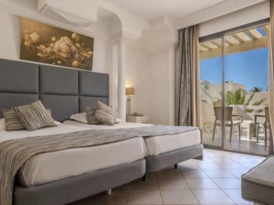 Světle zařízený hotelový pokoj se dvěma jednolůžky a balkonem s výhledem.