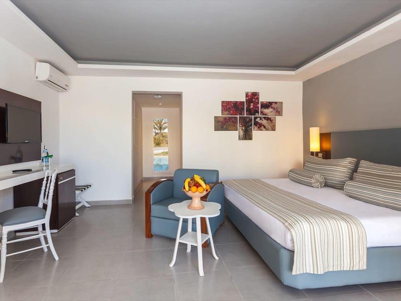 Moderně zařízený hotelový pokoj s velkou manželskou postelí, křeslem a psacím stolem.