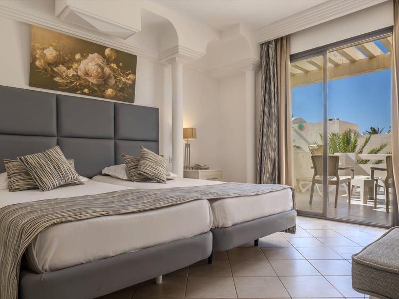 Světle zařízený hotelový pokoj se dvěma jednolůžky a balkonem s výhledem.