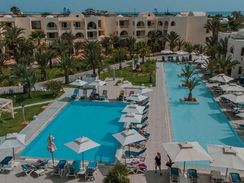 Pohled na dva bazény v hotelovém resortu s slunečníky a lehátky.