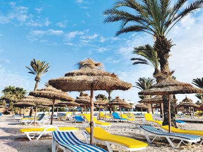 Plage avec parasols en paille et chaises longues sous un ciel bleu.