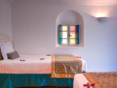 Hell beleuchteter Hotelraum mit zwei Betten und einem kleinen Fenster mit bunten Scheiben.