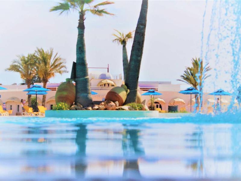 Vue sur une piscine avec des palmiers et des transats en arrière-plan sur la plage.