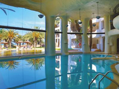 Kryty basen wewnętrzny z widokiem na palmy i odkryte baseny.