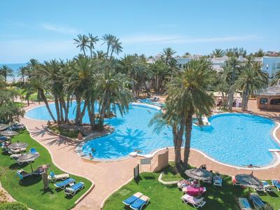 Großer Pool mit Palmen, Liegestühlen und Blick auf das Meer in einem Hotelresort.