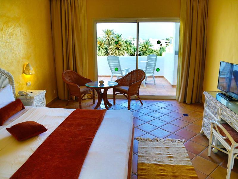 Przytulny pokój hotelowy z łóżkiem podwójnym, tarasem i widokiem na palmy.