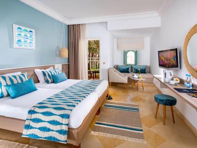 Modern eingerichtetes Hotelzimmer mit Doppelbett, Sitzbereich und TV an der Wand.