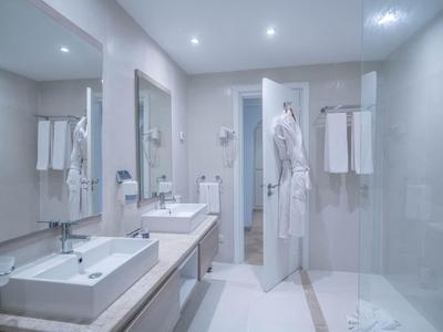 Modernes Hotelbadezimmer mit zwei Waschbecken und Bademänteln an der Tür.