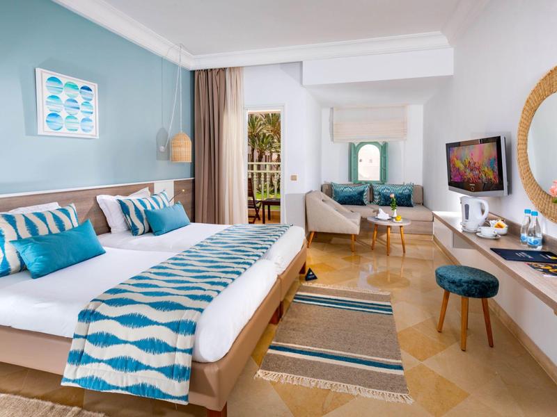 Modern eingerichtetes Hotelzimmer mit Doppelbett, Sitzbereich und TV an der Wand.