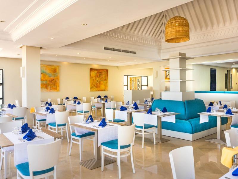 Heller, moderner Gastraum mit weißen Stühlen, blauen Sitzpolstern und blauen Servietten auf Tischen.