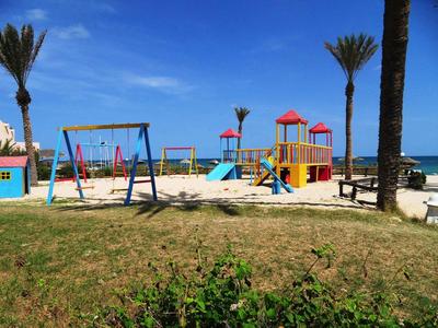 Kinderspielplatz mit Schaukeln und Rutschen am grünen Gras unter blauem Himmel.