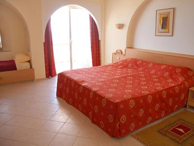 Camera da letto con letto matrimoniale, tende rosse e un piccolo angolo salotto vicino a una finestra ad arco.