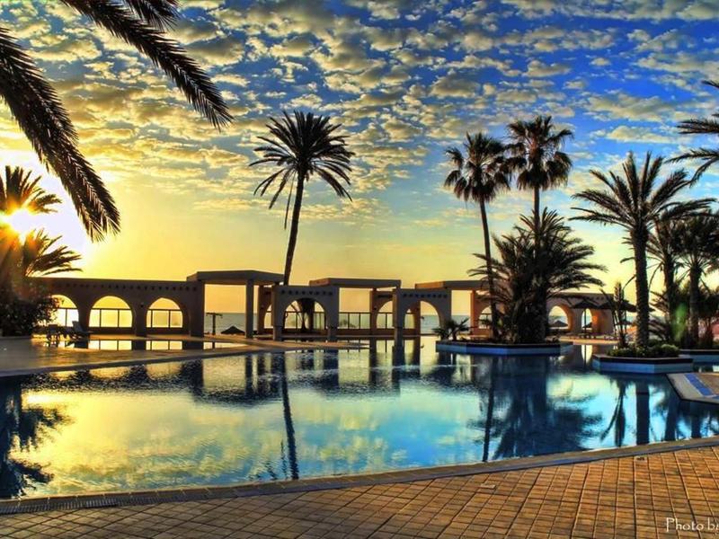 Zachód słońca nad luksusowym basenem z palmami i miejscami do siedzenia na zewnątrz.