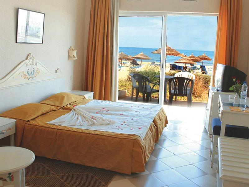 Chambre d'hôtel avec lit double, terrasse et vue sur la mer avec parasols sur la plage.