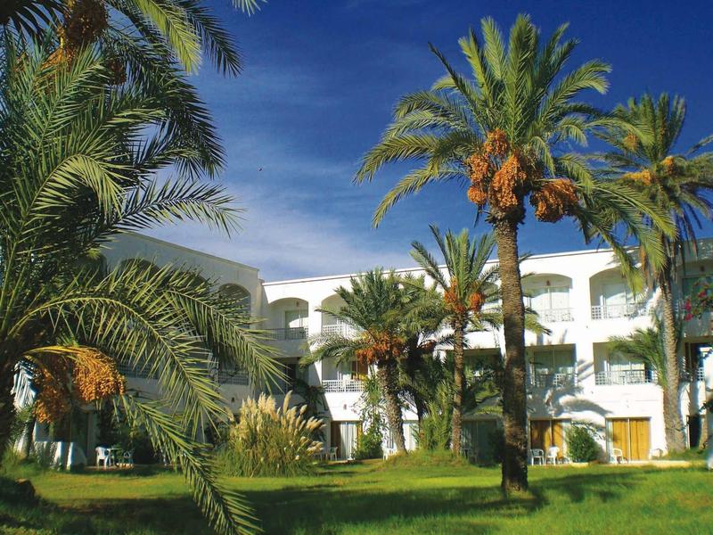 Bâtiment d'hôtel blanc derrière de grands palmiers sous un ciel clair.