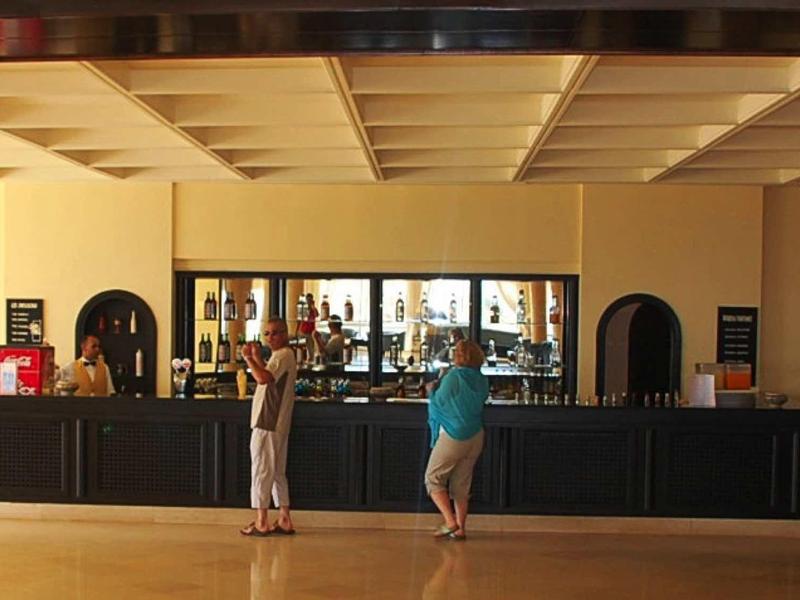 Bar d'hôtel avec barman et clients commandant des boissons et discutant.