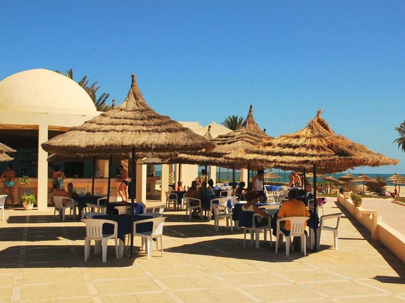 Terrasse ensoleillée avec parasols en paille et tables dans un complexe ensoleillé