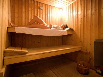 In einer Sauna liegt eine Frau auf einer oberen Holzbank, umgeben von warmem Holzinterieur.