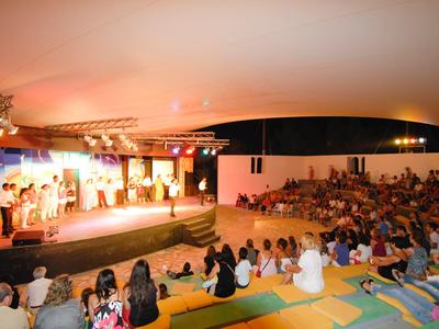 Großes Publikum sitzt in einem farbenfrohen Amphitheater und schaut auf eine beleuchtete Bühne.