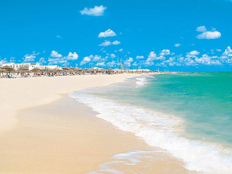 Bílá písčitá pláž s tyrkysovou vodou a jasně modrou oblohou.