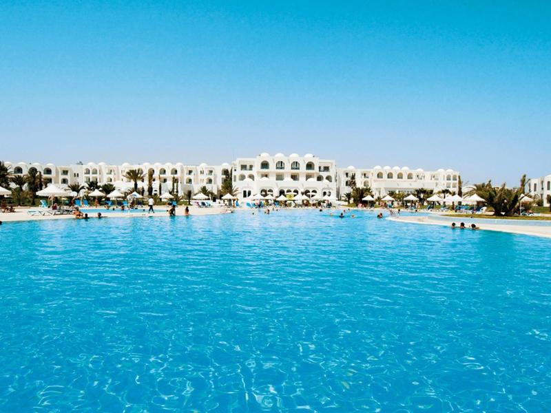 Velký modrý bazén před bílým hotelem pod jasnou oblohou.