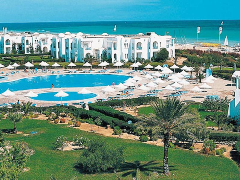 Pohled na hotelový komplex s bazénem, trávníkem a výhledem na moře v dálce.