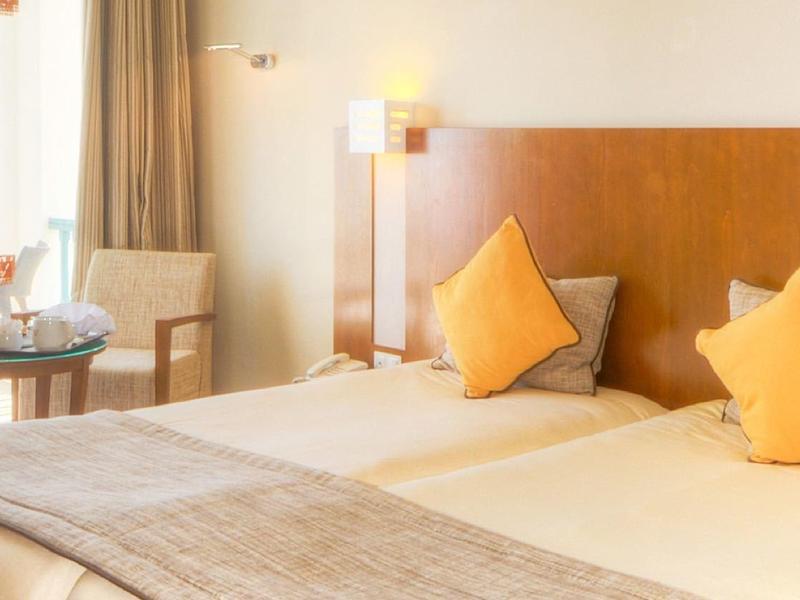 Světý hotelový pokoj s manželskou postelí a výhledem na zahradu a moře.