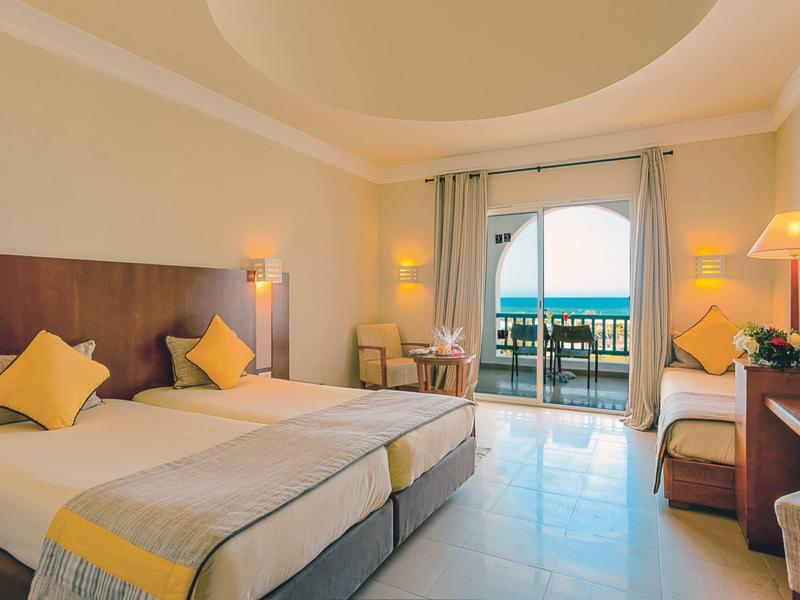 Světý pokoj hotelu se dvěma lůžky, balkon s výhledem na moře, světlý nábytek a minimalistická výzdoba.