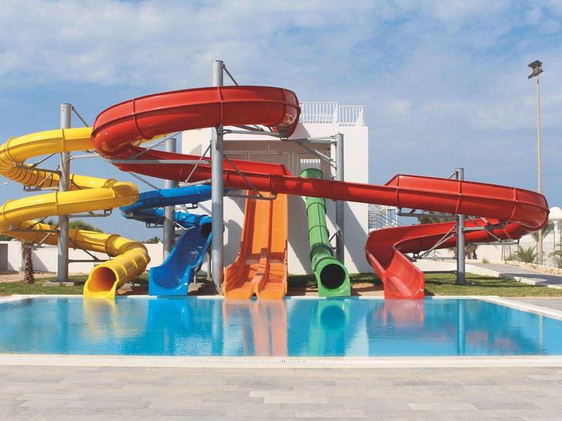 Barevné tobogány u venkovního bazénu hotelového areálu za slunečného dne.