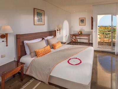 Helles Schlafzimmer mit großem Bett, Holzmöbeln, Teppich und Balkon mit Meerblick.