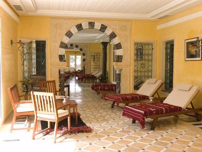 Heller Raum mit gelben Wänden, gemustertem Boden, mehreren Liegestühlen und Holztischen.