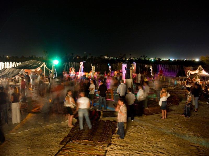 Menschen tanzen nachts auf einem beleuchteten Festplatz mit Zelten im Hintergrund.