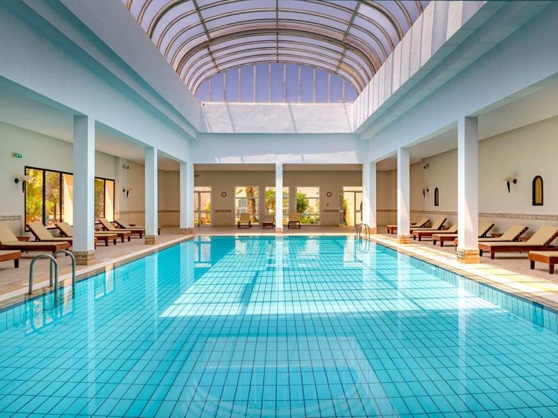 Heller, rechteckiger Hallenbad mit klarem Wasser, Liegestühlen und Glasdach.