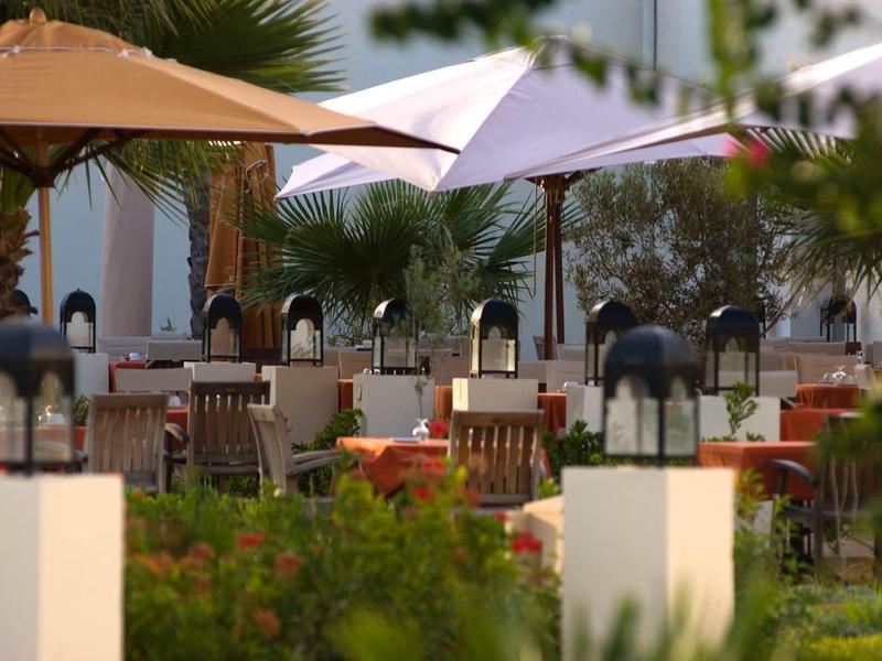 Einladende Außenterrasse mit Tischen, Stühlen und großen Sonnenschirmen umgeben von Grün.