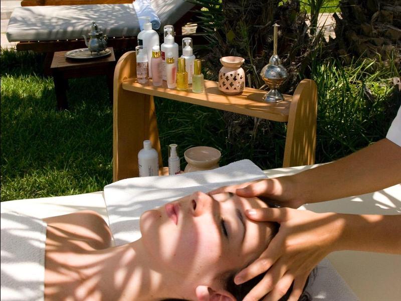 Person entspannt sich auf Liege beim Wellness, Hände massieren Gesicht in sonnigem Gartenbereich.