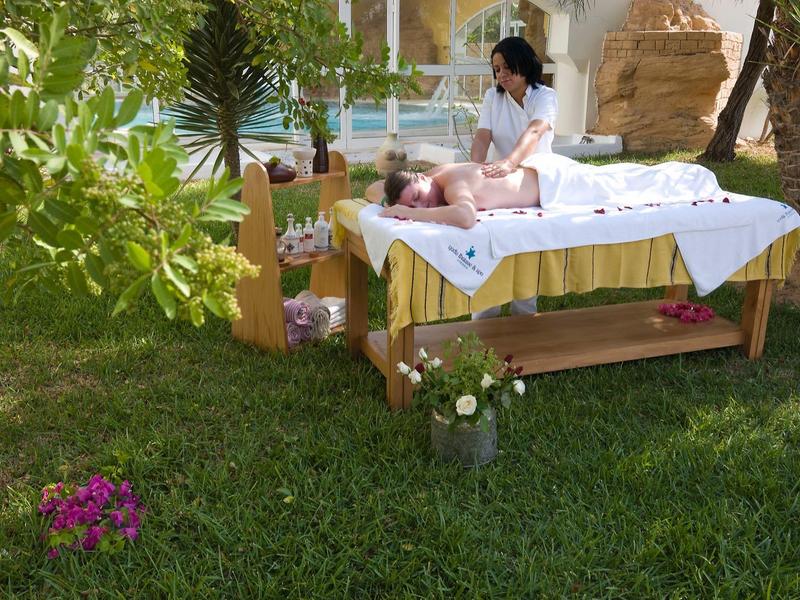 Frau massiert auf Massagebank im Garten, umgeben von Blumen und grünen Pflanzen.