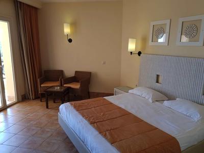 Hotelový pokoj s manželskou postelí, dvěma křesly a třídílnou dekorací na stěně v teplých odstínech.