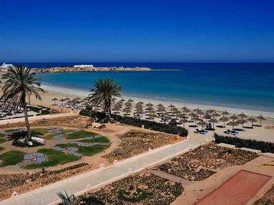 Hotel sulla spiaggia con lettini, palme e mare limpido sotto un cielo blu.