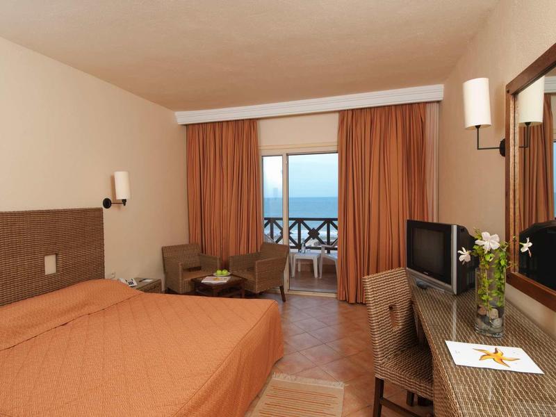 Camera d'hotel con letto matrimoniale, TV, scrivania e balcone con vista sul mare.