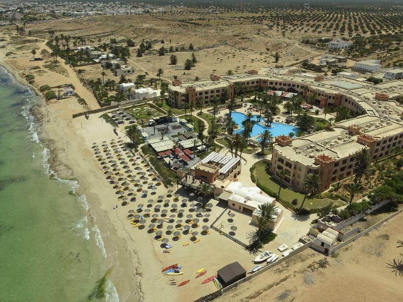 Complesso alberghiero con piscina e ombrelloni sulla spiaggia in una zona arida e sabbiosa