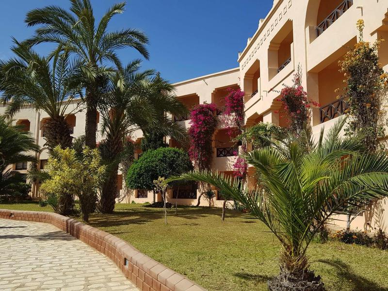 Hotel con edifici gialli circondati da palme e verde curato sotto un cielo sereno.