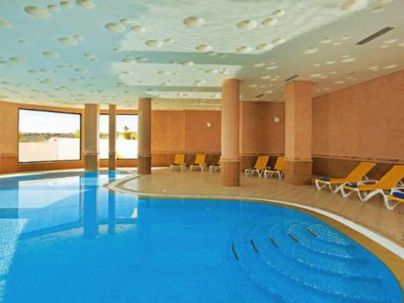 Area interna con grande piscina e lettini in una stanza luminosa e moderna.