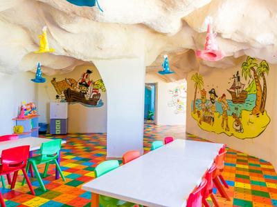 Area giochi per bambini con pavimento colorato, tavoli e sedie in design a parete di grotta.