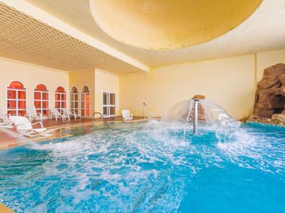Piscina interna con cascata e lettini in area benessere luminosa dell'hotel.