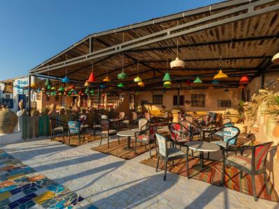 Area ristorante all'aperto dell'hotel con tavoli, sedie e lampade colorate sotto un tetto in legno alla luce del sole