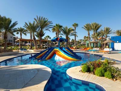 Piscina con scivolo colorato in resort tropicale con palme e sole.